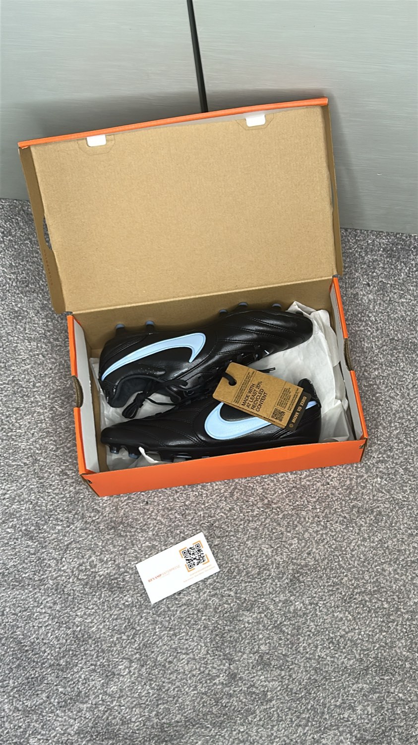 Black Nike football boots with a light blue swoosh in their orange box